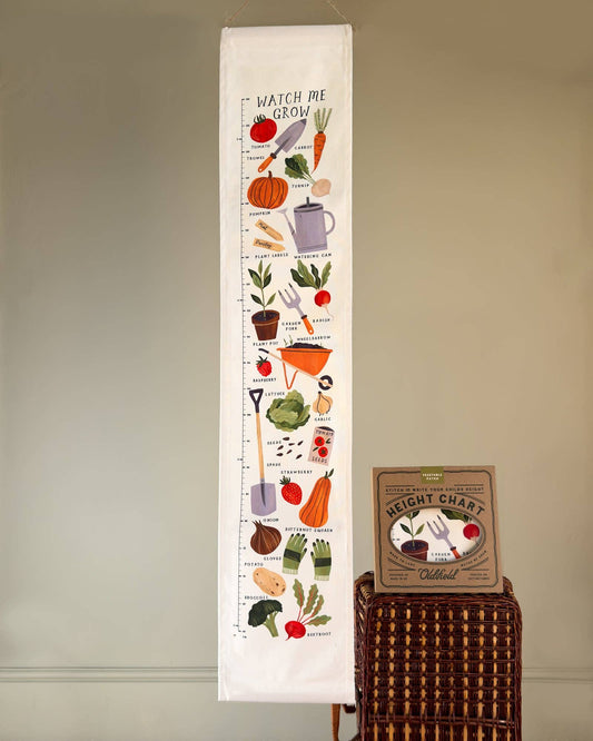 A cotton canvas fabric children's height chart printed with a colourful Vegetable Patch illustration. It is hanging on a wall next to a packaged height chart.