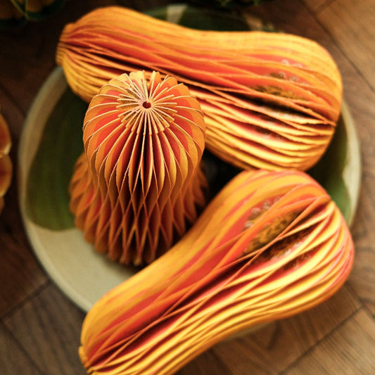 Three-dimensional honeycomb squash decorations arranged in a bowl with pumpkin decorations nearby.