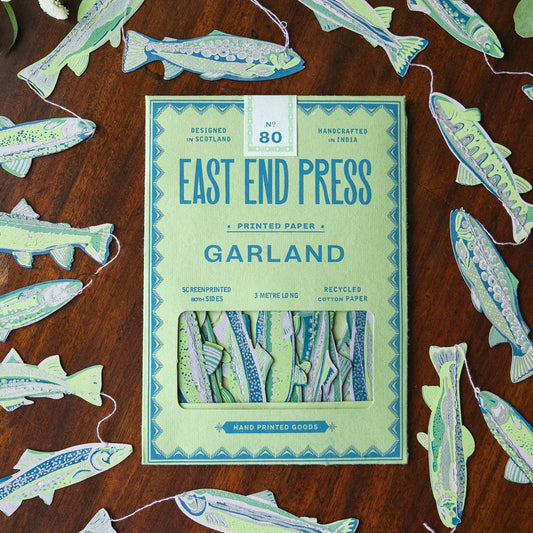 A colourful hand printed paper garland of anchovies, packaged in an East End Press branded envelope, surrounded by another unfolded garland.