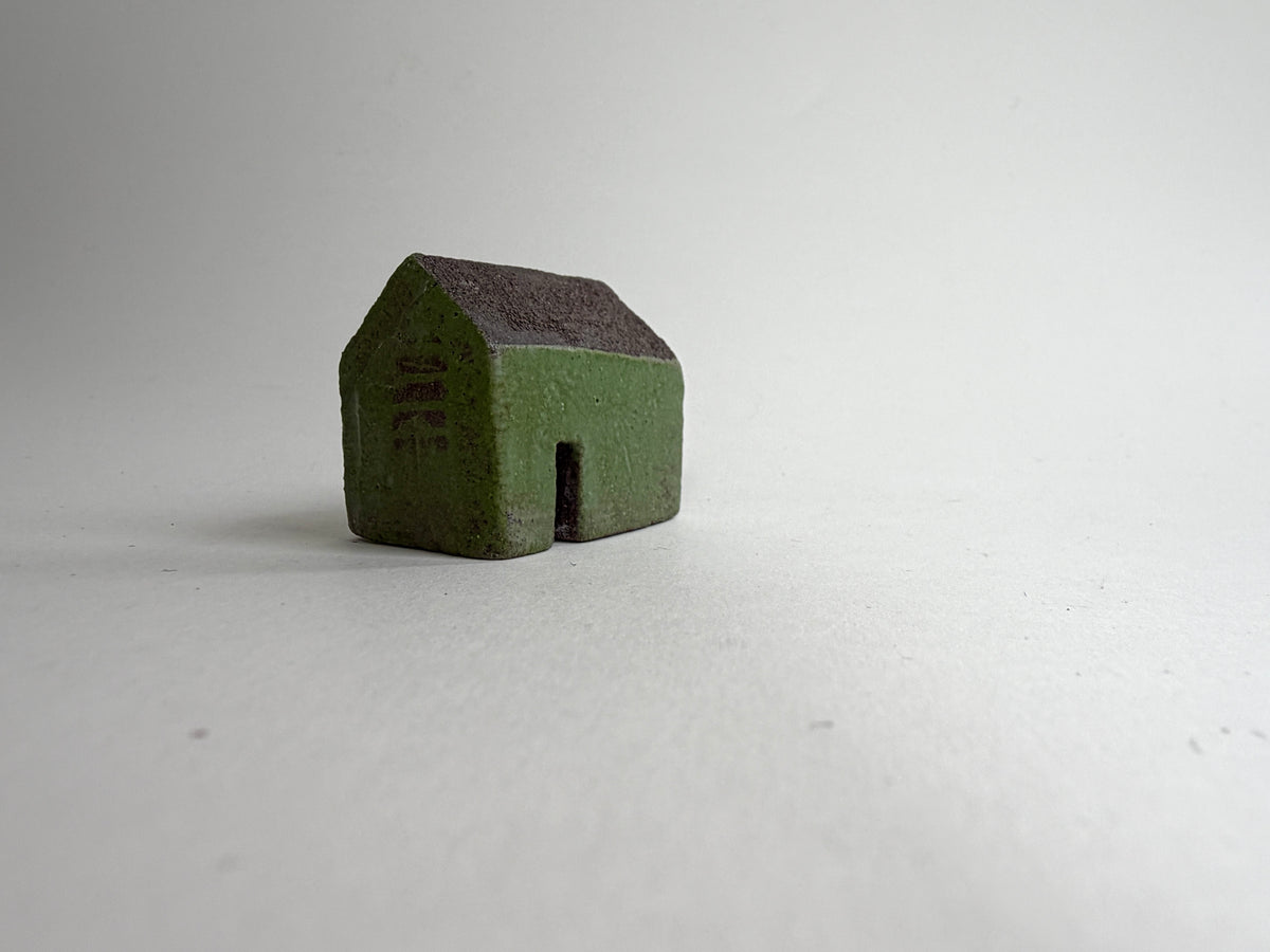 A small decorative ceramic house ornament shown against a plain light gray background.