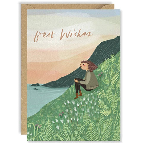 An A6 greeting card with kraft envelope featuring a colourful illustration by Joy Nevada of a person sitting on hill with ferns, and the words 'Best Wishes'.
