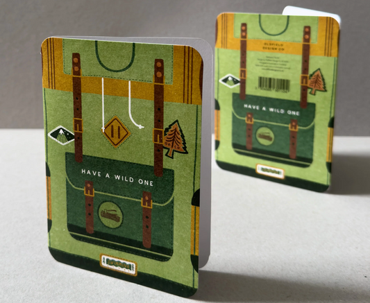 2 standing greeting cards with rounded edges showing the front and back designs. Both have a full coverage illustration of a green backpack with patches, straps and pocket and the words 'Have a wild one'.