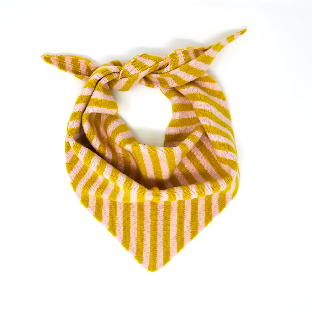 A Scarlet Knitwear brand lambswool triangle scarf with a light pink and mustard stripe design, arranged as it would be worn.