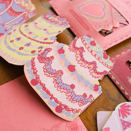 A concertina card with illustrated tiered birthday cakes displayed over more East End Press designs.