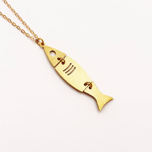 A gold fish-shaped pendant necklace on a delicate gold chain, photographed on a clean white background.