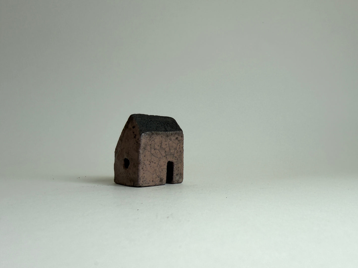 small ceramic house in a mocha-brown against a grey background