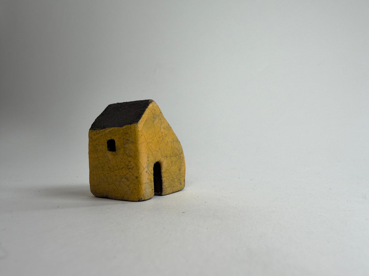 A small decorative ceramic house ornament shown against a plain light gray background.