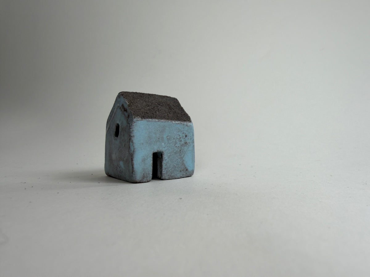 A small decorative ceramic house ornament shown against a plain light gray background.