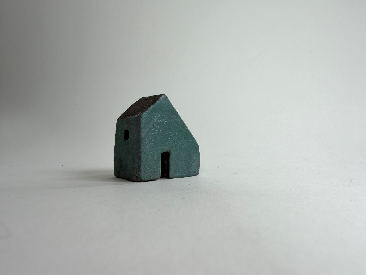 A small decorative ceramic house ornament shown against a plain light gray background.