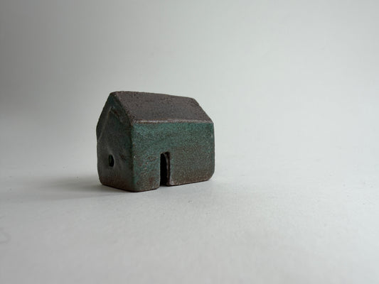 A small decorative ceramic house ornament shown against a plain light gray background.