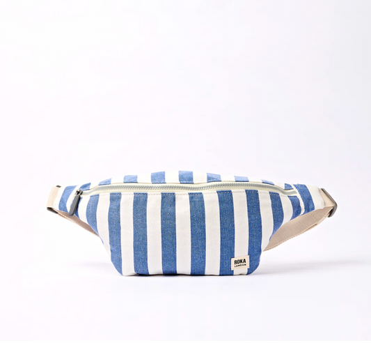 A blue and white striped canvas sling bag with a beige adjustable strap and a small 'ROKA' brand label on the front, set against a plain white background.