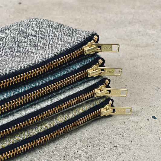A stack of four small square coin purses made from single origin Iona Tweed in natural colours and patterns with brass zips. 